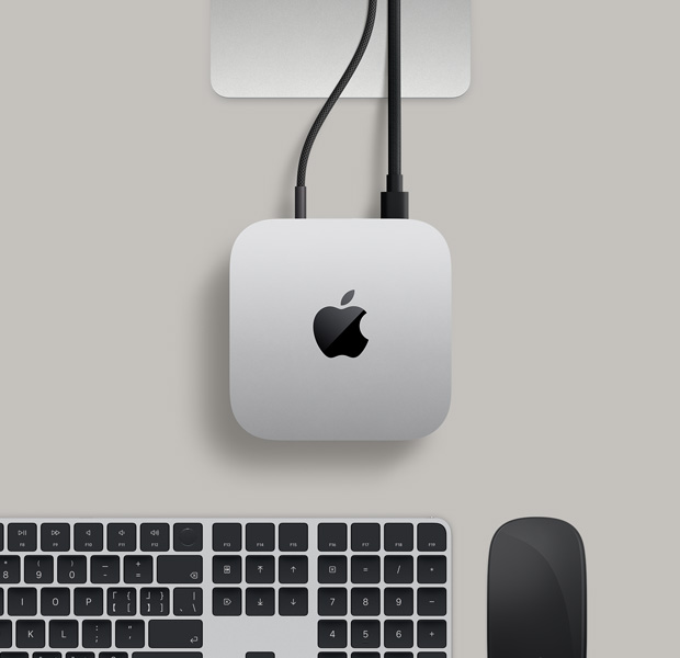 银色 Mac mini 的俯视图,两条插入背面端口的连接线连接至一台显示器,旁边有黑色妙控鼠标和黑色妙控键盘。